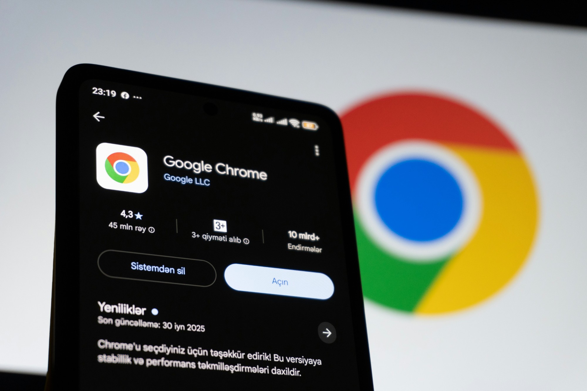 A phone showing the Google Chrome app listing, with the Chrome logo on a screen behind it
